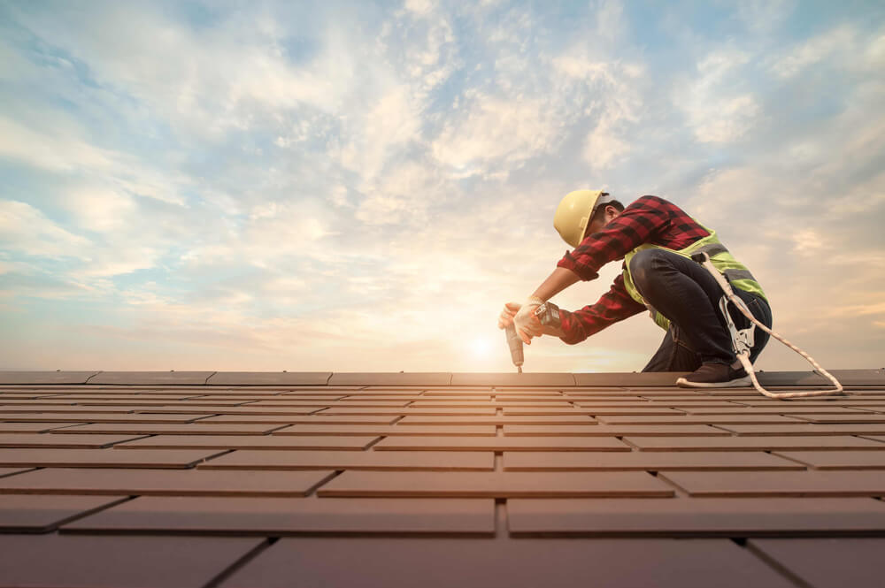 roofing worker at sunrise, drilling in shingles